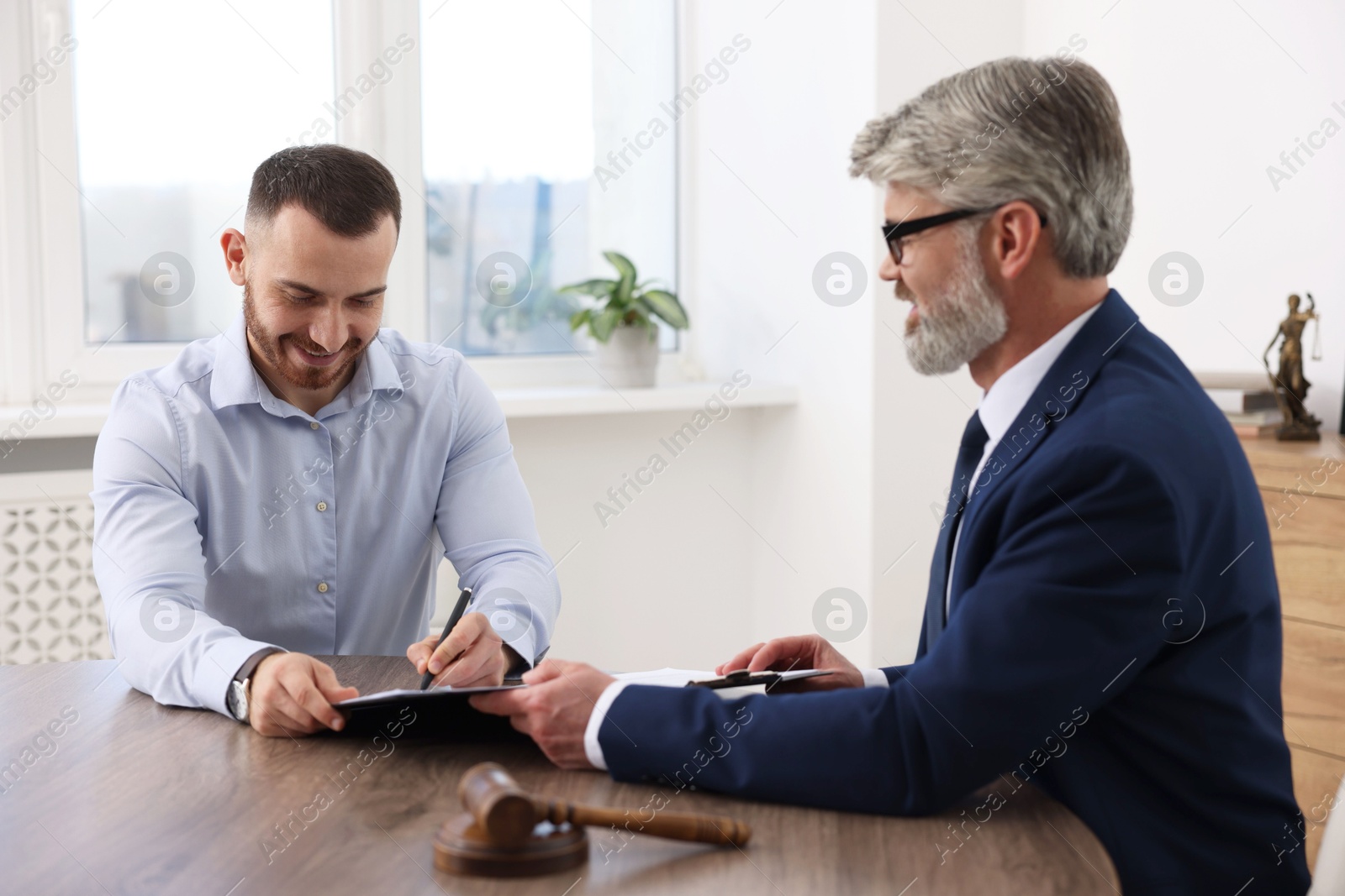 Photo of Client signing notarial paperwork during meeting with lawyer at wooden desk indoors, selective focus