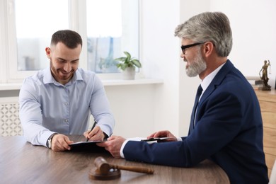 Client signing notarial paperwork during meeting with lawyer at wooden desk indoors, selective focus