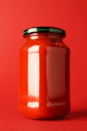 Photo of Ketchup in glass jar on red background