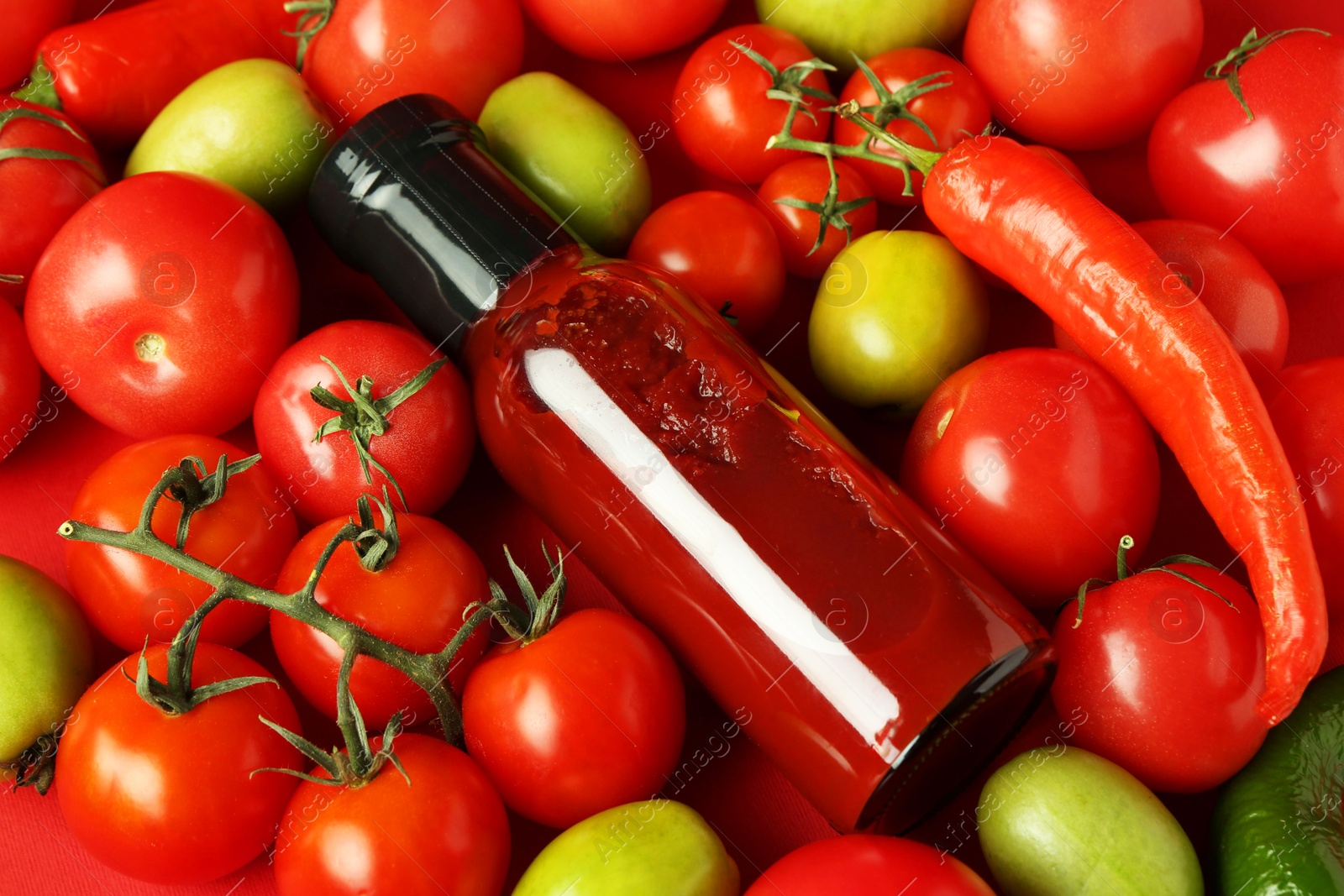 Photo of Tasty ketchup in bottle, chili and fresh tomatoes on red background, above view