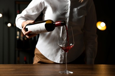 Photo of Professional sommelier pouring red wine into glass at wooden table indoors, closeup