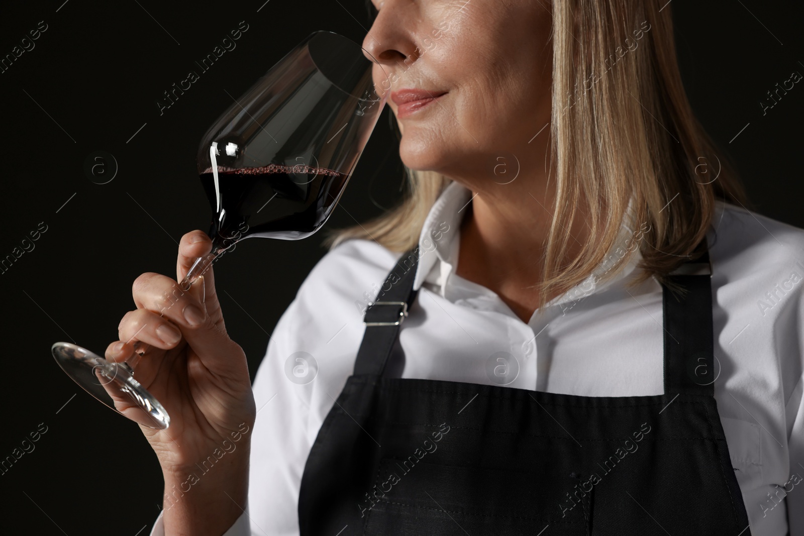 Photo of Professional sommelier tasting red wine in glass on black background, closeup