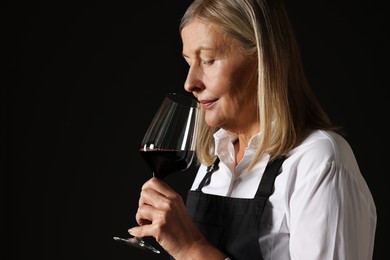 Photo of Professional sommelier tasting red wine in glass on black background