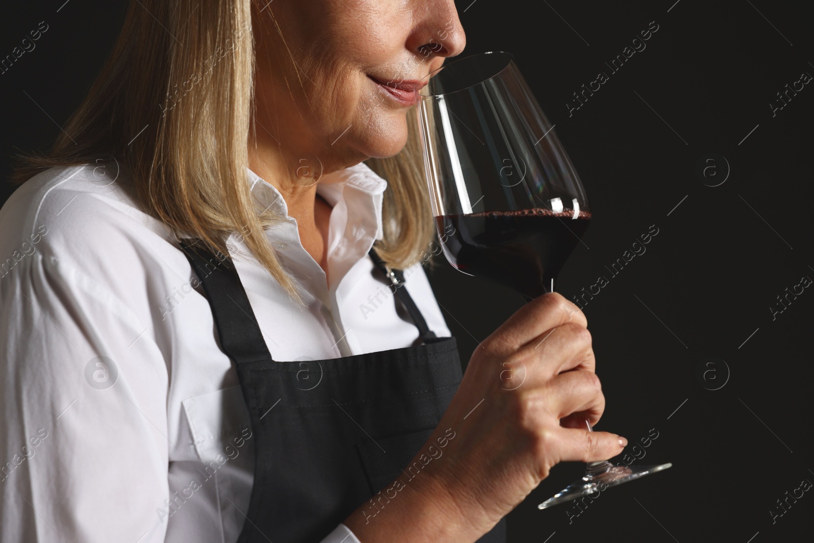 Photo of Professional sommelier tasting red wine in glass on black background, closeup