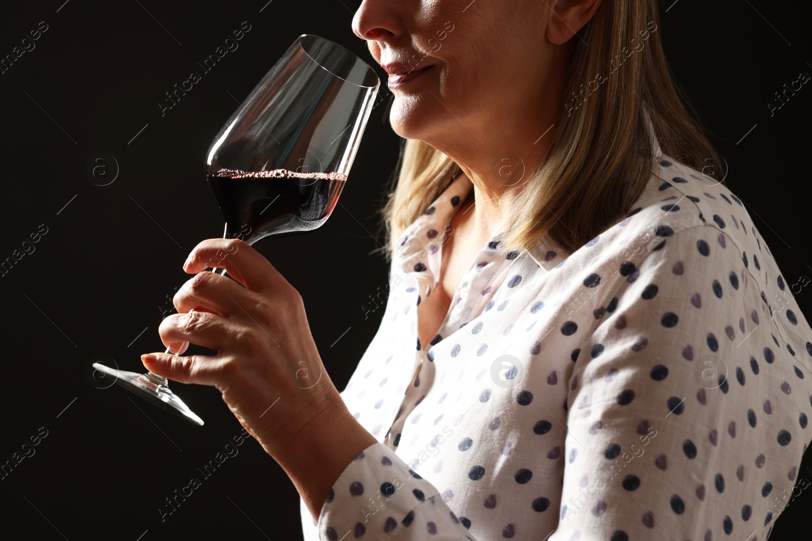 Photo of Professional sommelier tasting red wine in glass on black background, closeup