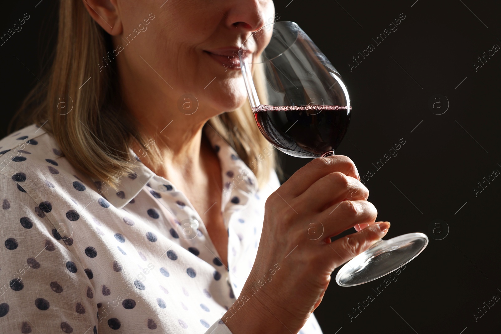 Photo of Professional sommelier tasting red wine in glass on black background, closeup