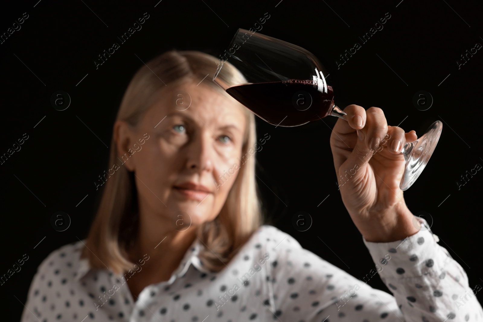 Photo of Professional sommelier analyzing quality of red wine on black background, selective focus