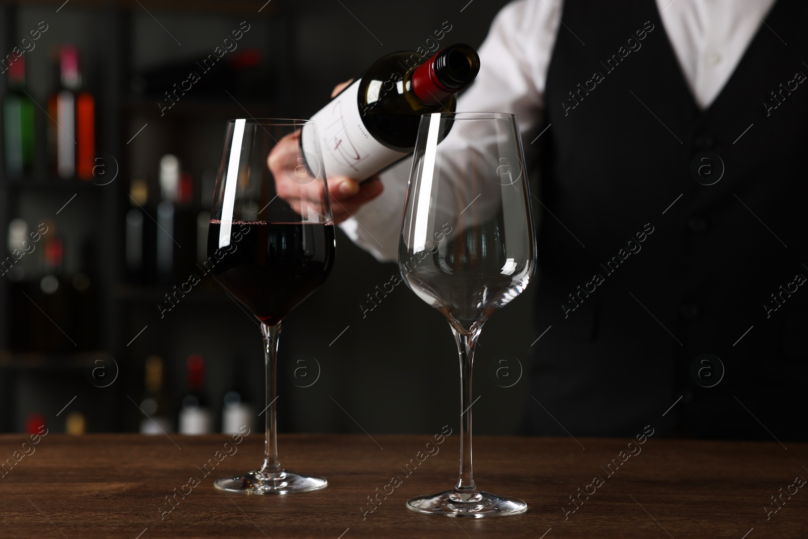 Photo of Professional sommelier pouring red wine into glasses at wooden table indoors, closeup