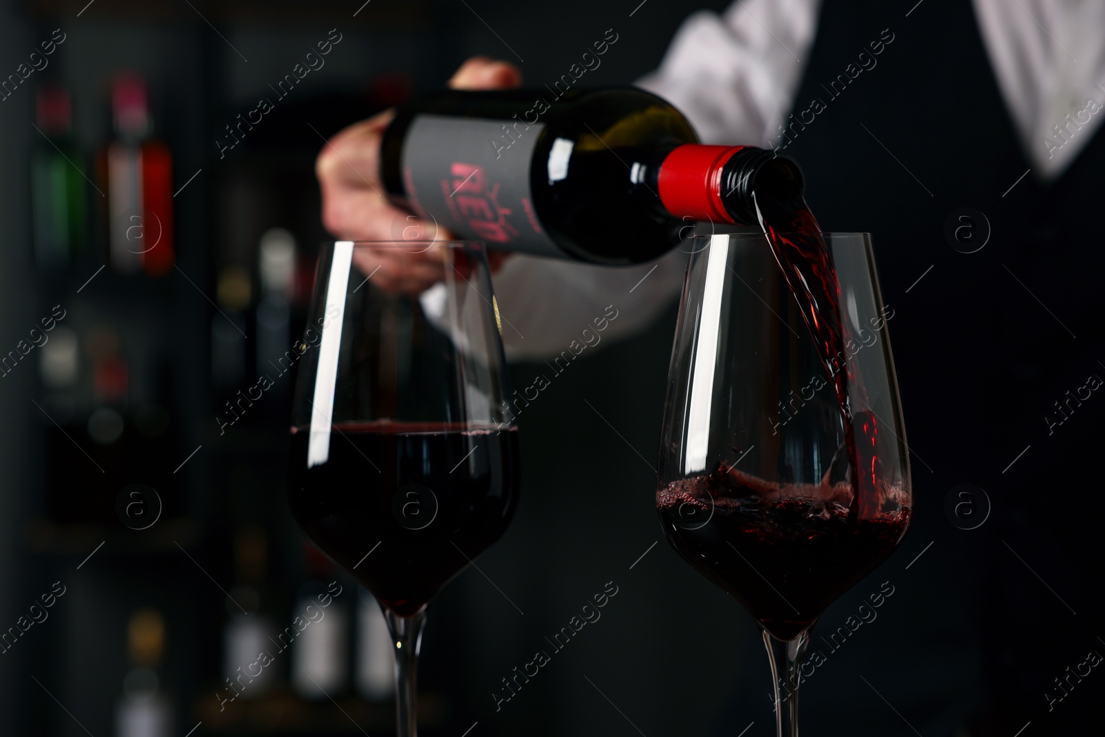 Photo of Professional sommelier pouring red wine into glasses indoors, closeup