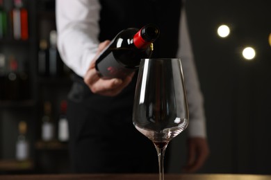 Photo of Professional sommelier pouring red wine into glass indoors, closeup