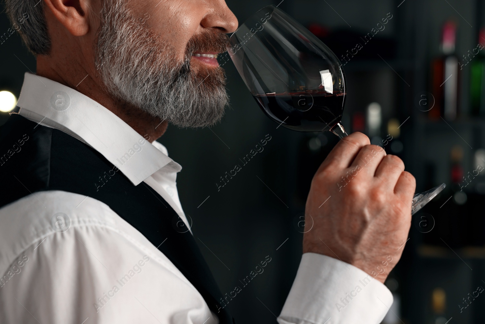 Photo of Professional sommelier tasting red wine indoors, closeup