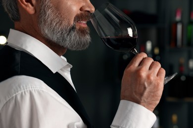 Professional sommelier tasting red wine indoors, closeup