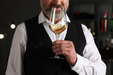 Professional sommelier tasting white wine in glass indoors, closeup