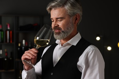 Photo of Professional sommelier tasting white wine in glass indoors