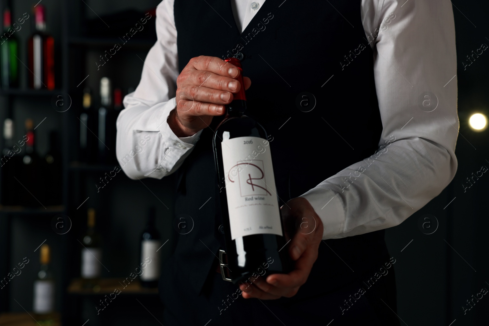 Photo of Professional sommelier holding bottle of red wine indoors, closeup