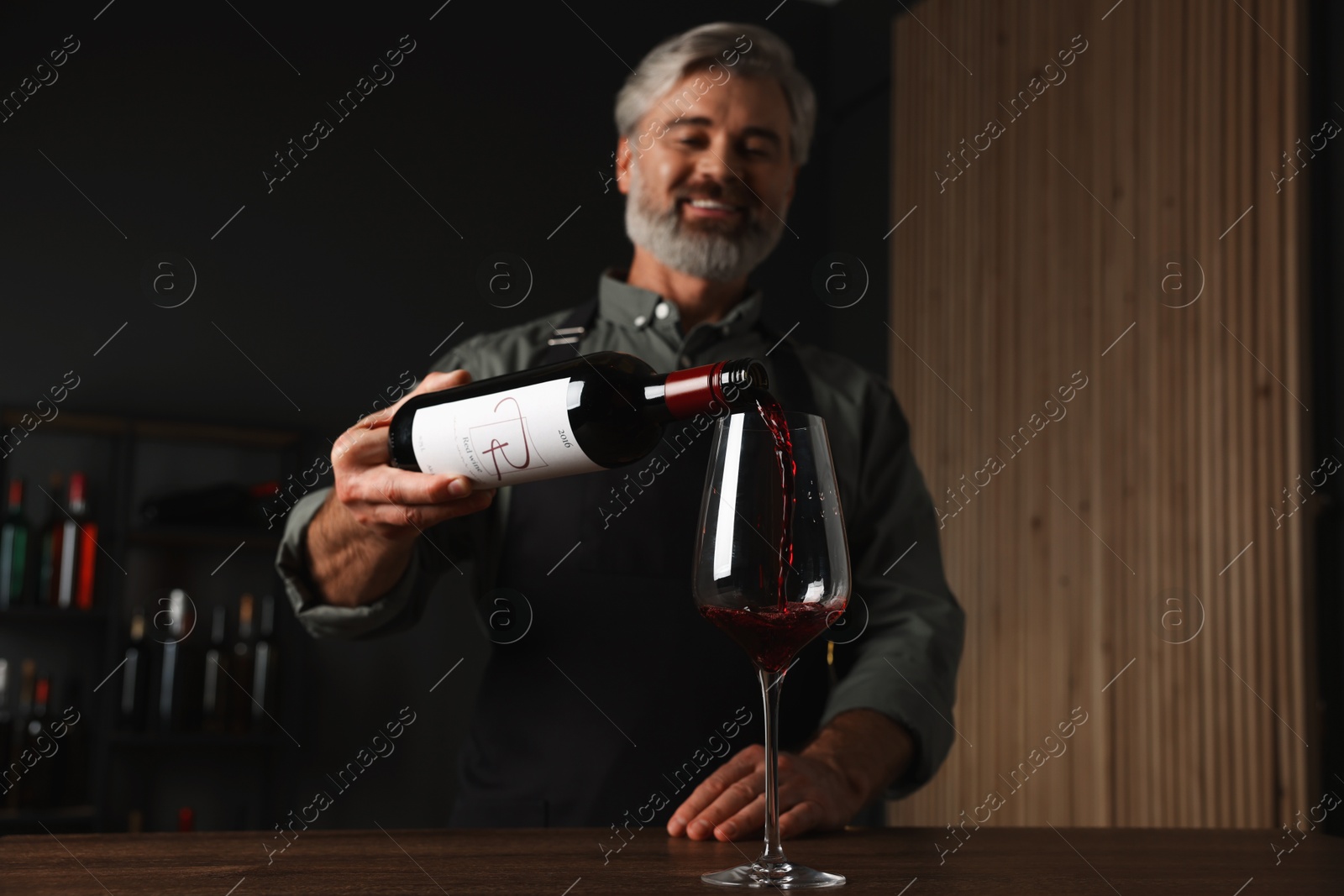 Photo of Professional sommelier pouring red wine into glass at wooden table indoors, selective focus