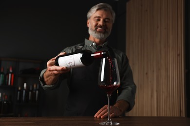 Professional sommelier pouring red wine into glass at wooden table indoors, selective focus