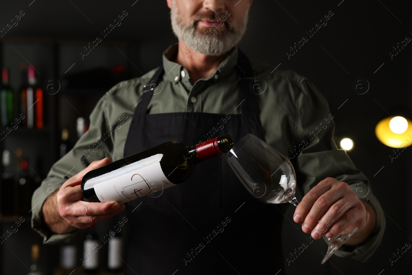 Photo of Professional sommelier pouring red wine into glass indoors, closeup