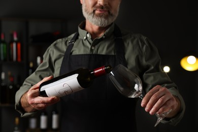 Professional sommelier pouring red wine into glass indoors, closeup