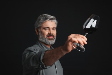 Photo of Professional sommelier analyzing quality of red wine on black background