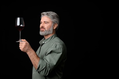 Professional sommelier analyzing quality of red wine on black background, space for text