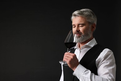 Professional sommelier tasting red wine on black background, space for text