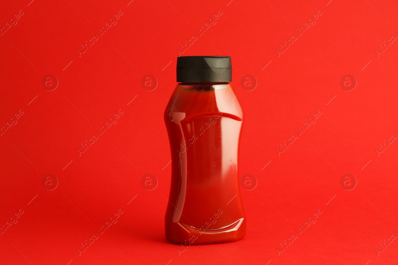 Photo of Ketchup in plastic bottle on red background