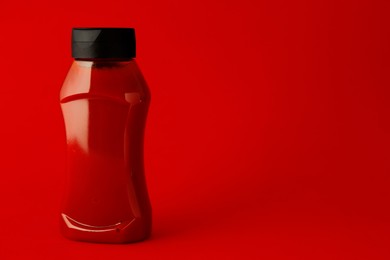 Photo of Ketchup in plastic bottle on red background. Space for text