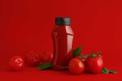 Photo of Bottle of ketchup and tomatoes on red background