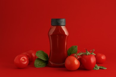 Photo of Bottle of ketchup and tomatoes on red background