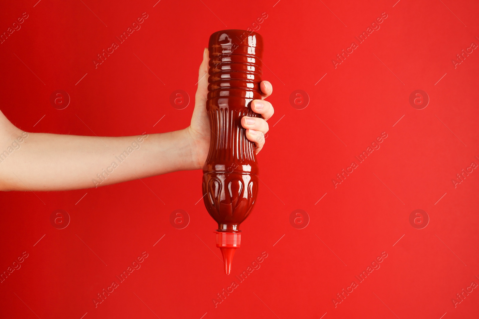 Photo of Woman squeezing ketchup out of bottle on red background, closeup