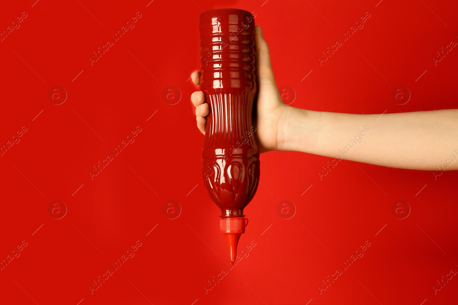 Photo of Woman squeezing ketchup out of bottle on red background, closeup