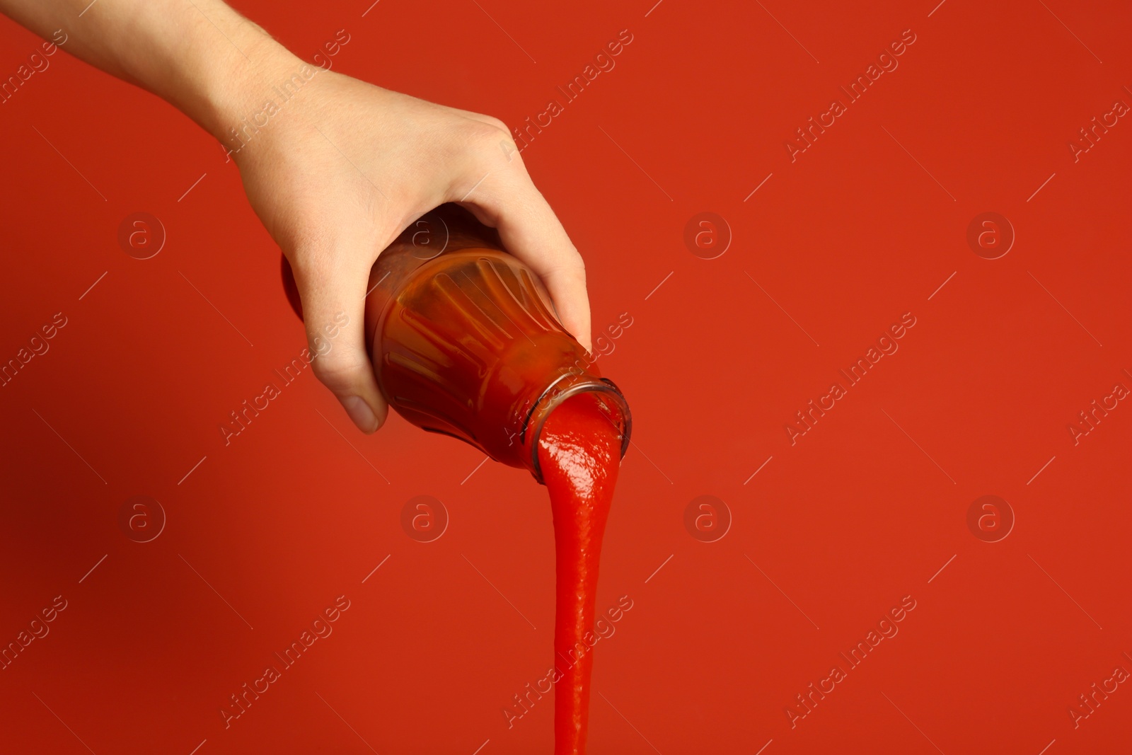 Photo of Woman pouring ketchup out of bottle on red background, closeup