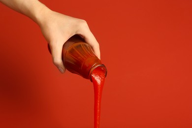 Photo of Woman pouring ketchup out of bottle on red background, closeup