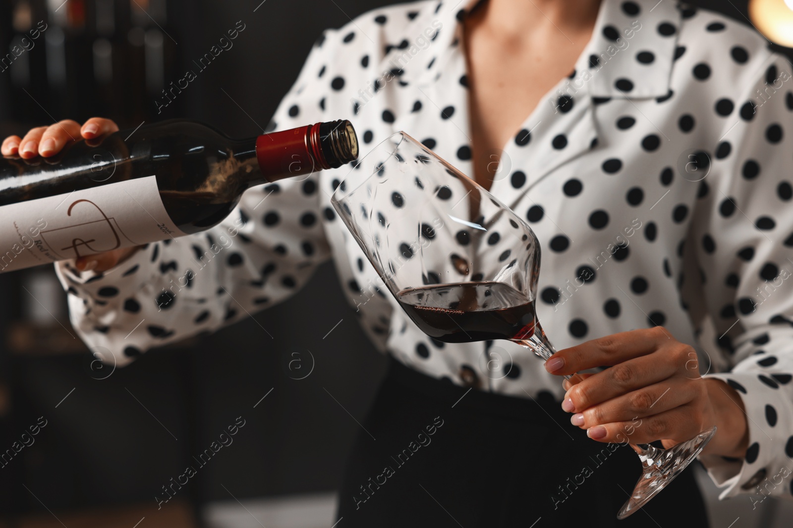 Photo of Professional sommelier pouring red wine into glass indoors, closeup