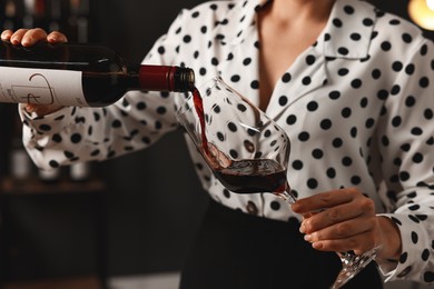 Photo of Professional sommelier pouring red wine into glass indoors, closeup