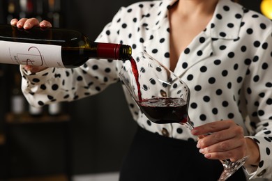 Photo of Professional sommelier pouring red wine into glass indoors, closeup