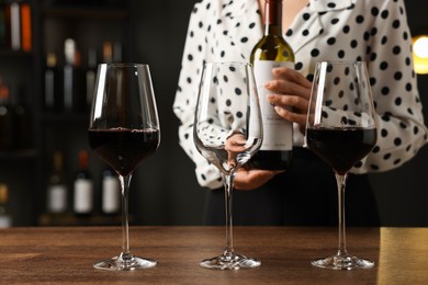 Photo of Professional sommelier with glasses and bottle of red wine at wooden table indoors, closeup