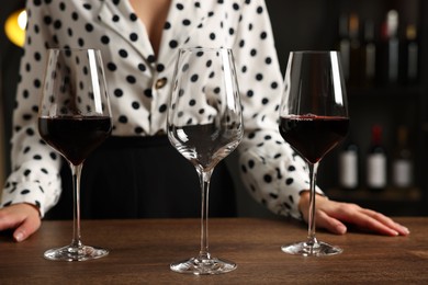 Photo of Professional sommelier with glasses of red wine at wooden table indoors, closeup