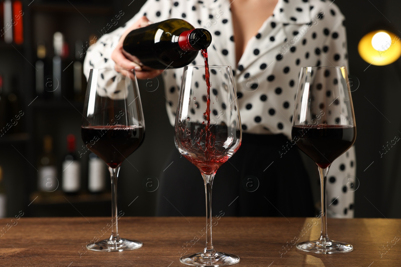 Photo of Professional sommelier pouring red wine into glasses at wooden table indoors, closeup