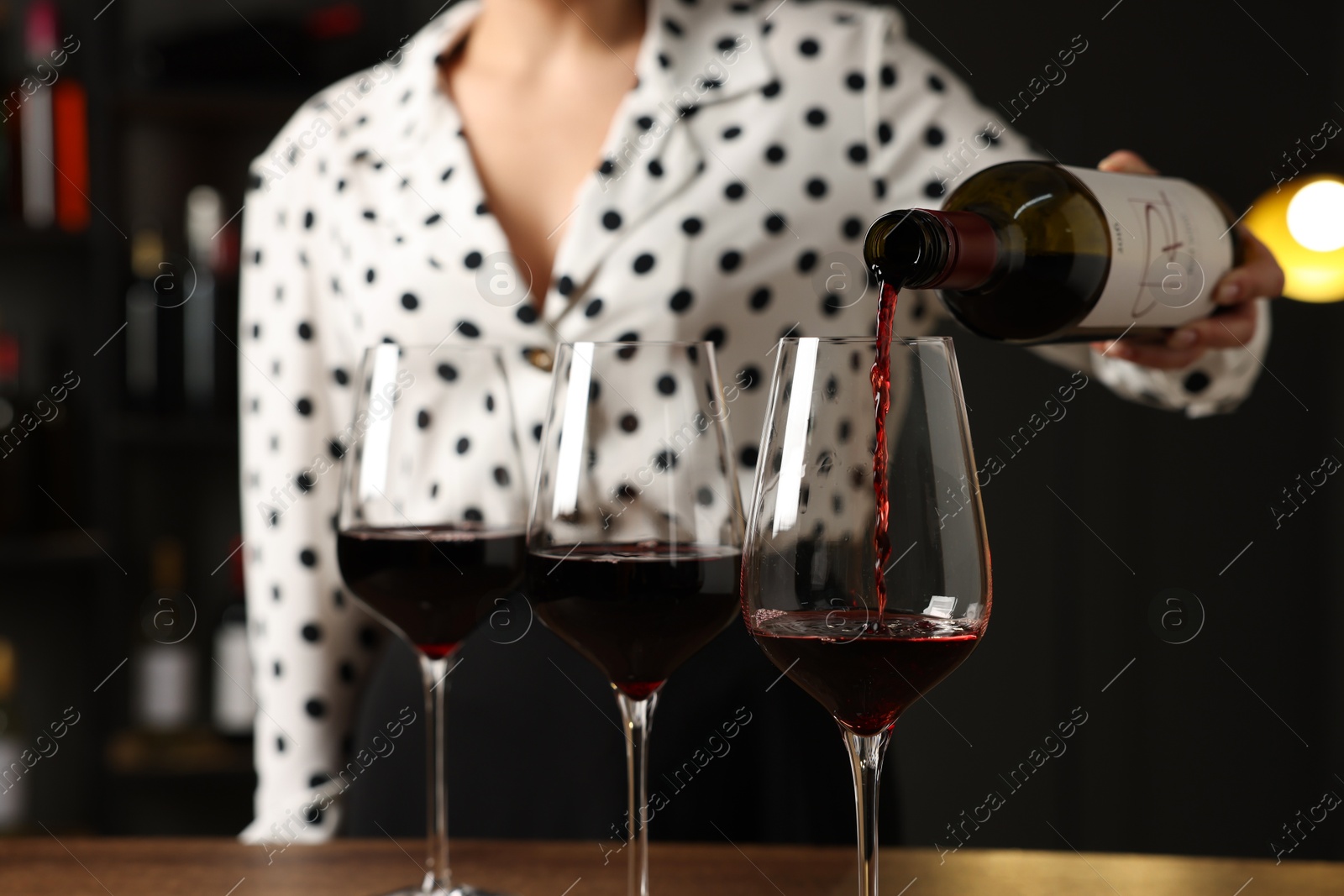 Photo of Professional sommelier pouring red wine into glasses at wooden table indoors, closeup