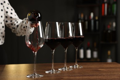 Photo of Professional sommelier pouring red wine into glasses at wooden table indoors, closeup