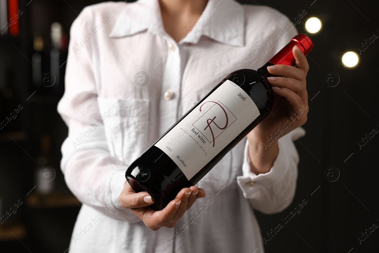 Photo of Professional sommelier holding bottle of red wine indoors, closeup