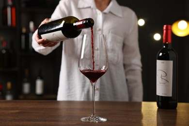 Photo of Professional sommelier pouring red wine into glass at wooden table indoors, closeup