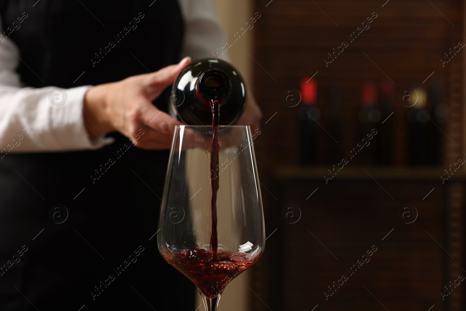 Photo of Professional sommelier pouring red wine into glass indoors, closeup