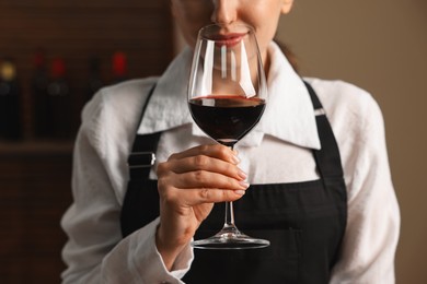 Photo of Professional sommelier tasting red wine in glass indoors, closeup