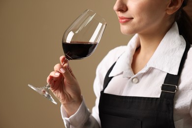 Photo of Professional sommelier tasting red wine in glass on beige background, closeup