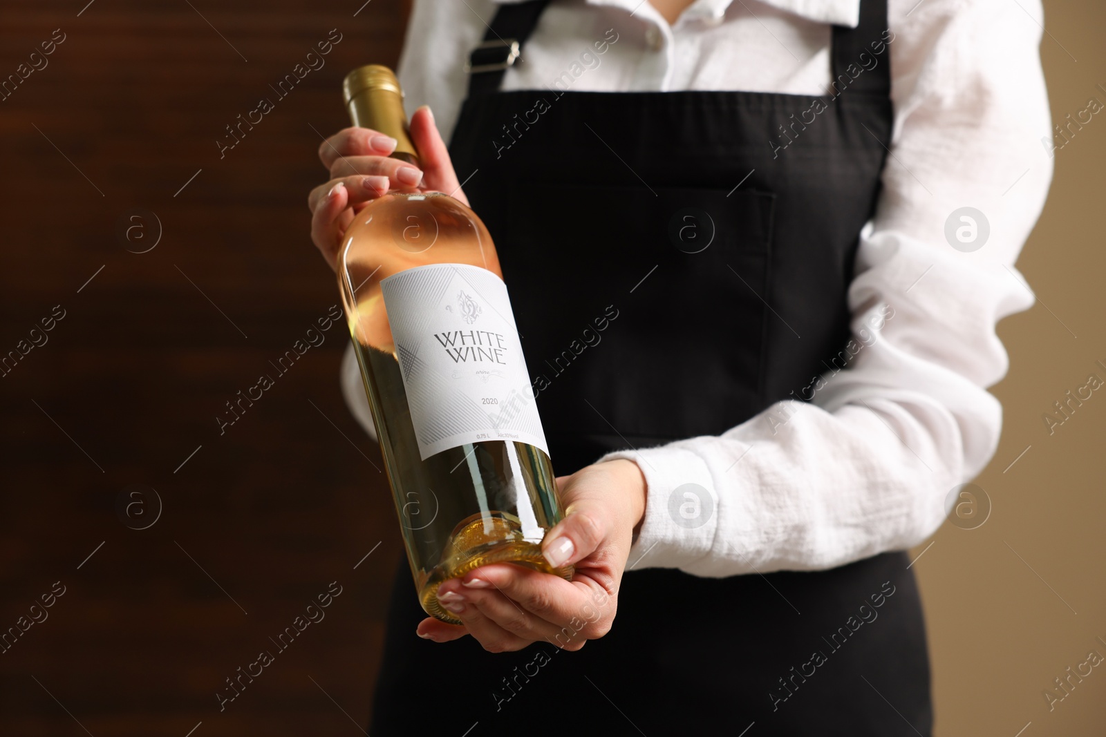 Photo of Professional sommelier holding bottle of white wine indoors, closeup