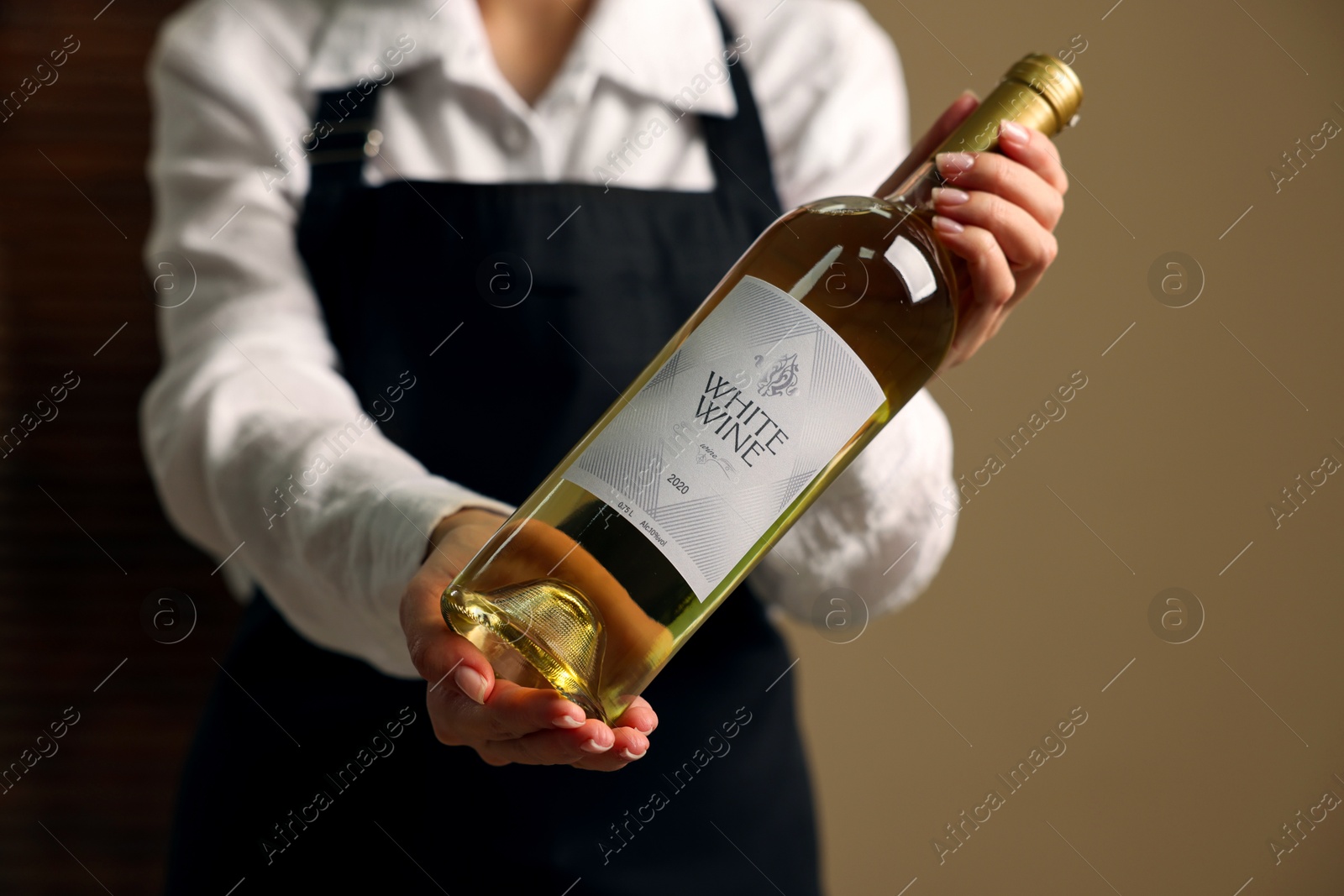 Photo of Professional sommelier holding bottle of white wine indoors, closeup