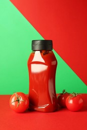 Photo of Bottle of ketchup and tomatoes on color background